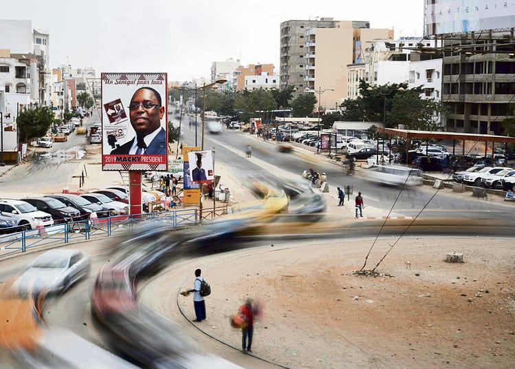 Vehicles move past a roundabout adorned with posters of Senegalese President Macky Sall in Dakar on February 19, 2019, ahead of scheduled presidential elections on February 24. - Former French colony Senegal, has been buffeted by violence ahead of the February 24 vote, which incumbent President Macky Sall hopes to win outright in the first round. (Photo by MICHELE CATTANI / AFP)