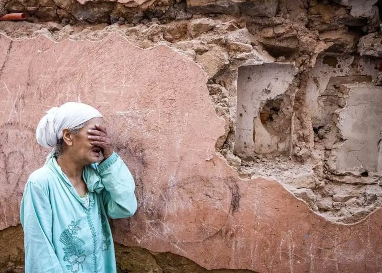 Vieille dame en pleurs près d'un immeuble en ruine